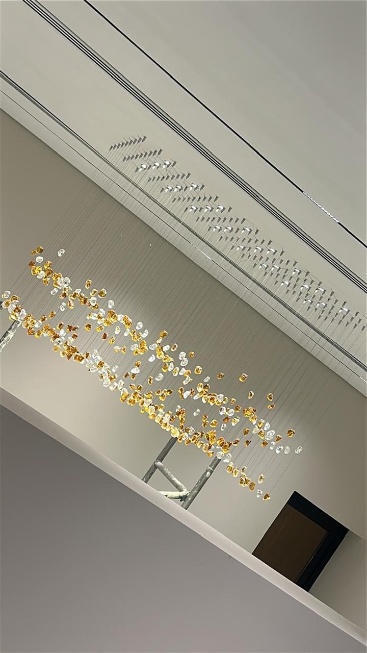 Cascade of crystal and gold pendant lights below a linear diffuser ceiling