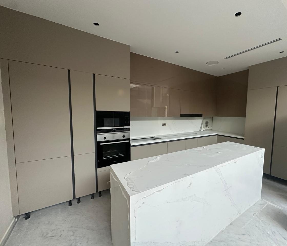 Handleless taupe kitchen with tall units, built-in ovens and a marble-effect island
