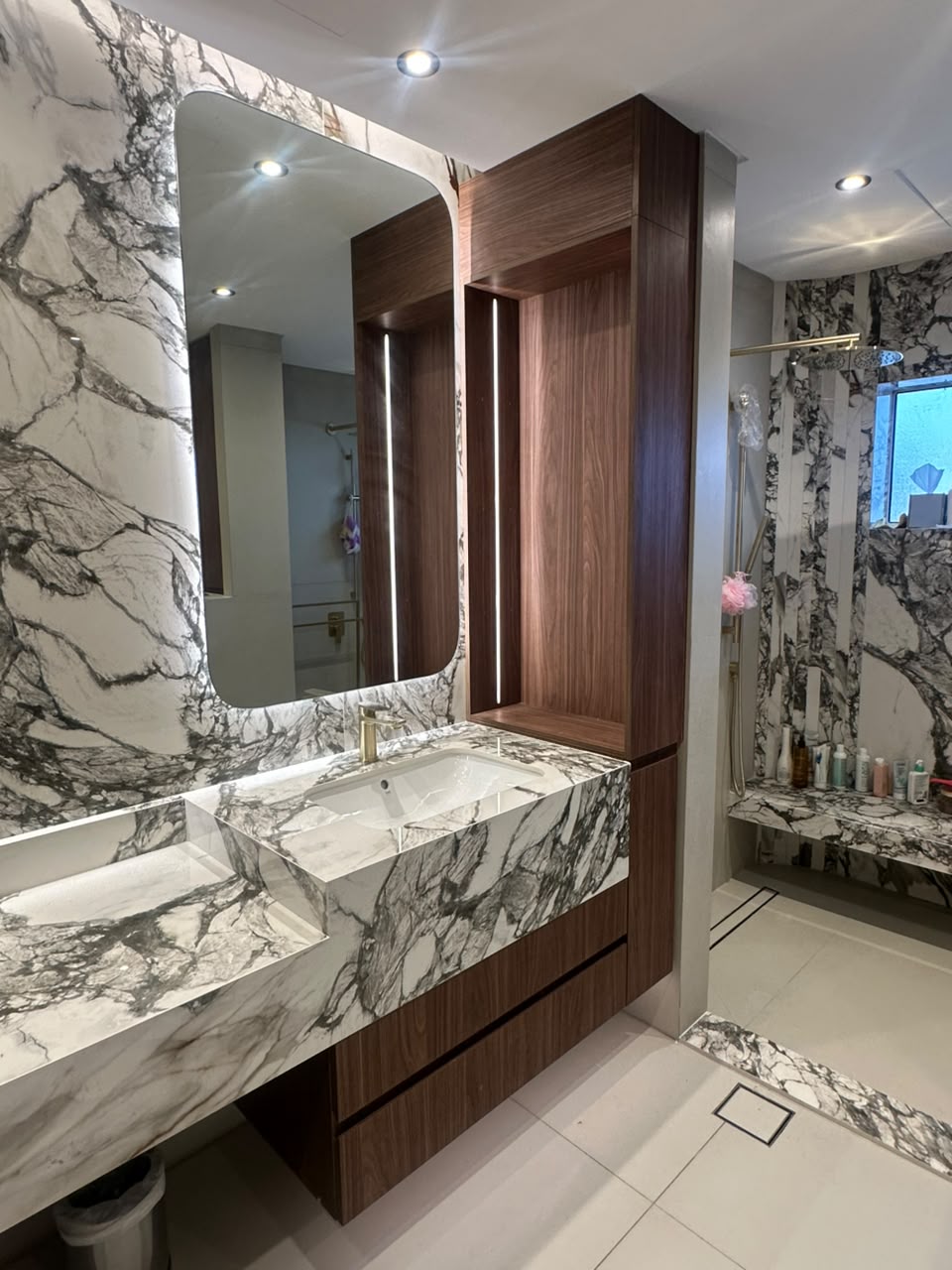 Bathroom with a floating walnut vanity, white-and-black marble basin and wall, backlit mirror and a lit walnut niche